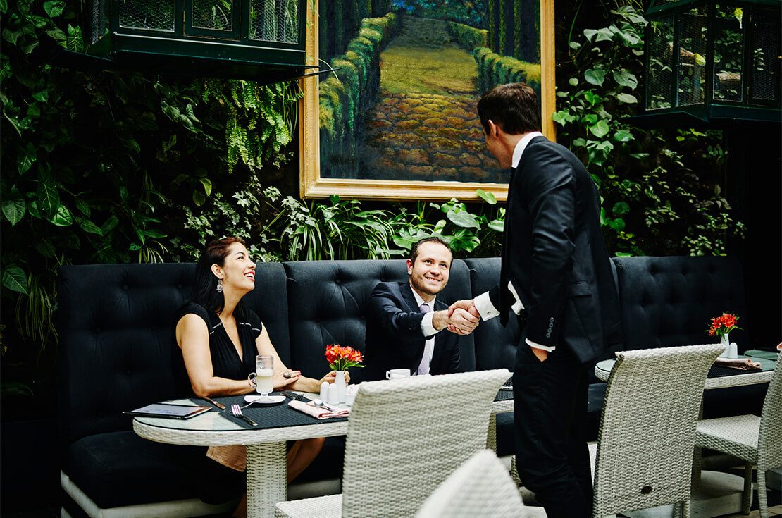 Smiling businessmen shaking hands before sitting down at table for meeting with business executives in restaurant