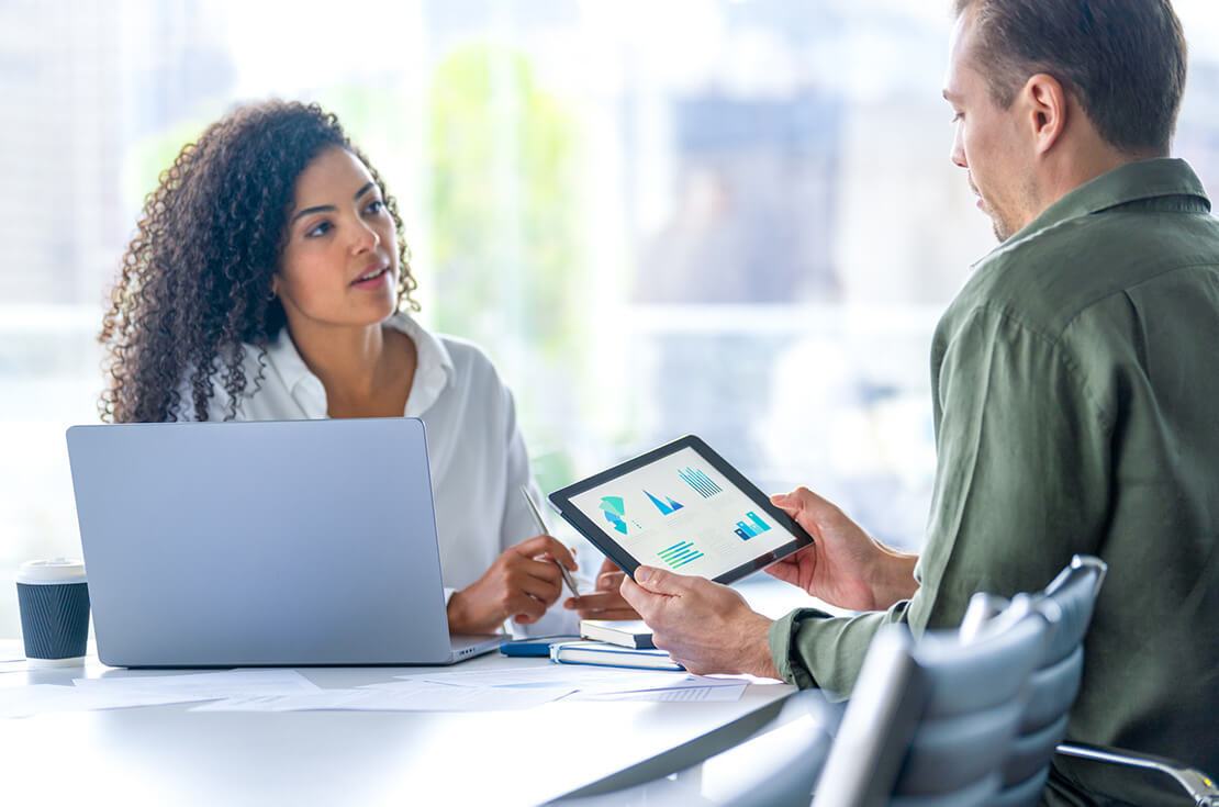 Business man and business woman in a meeting at the office. There is a laptop on the table and the man is holding a digital tablet with finance chart and graphs