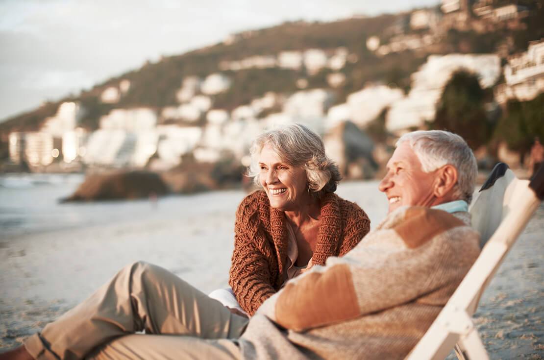 Happy senior couple relaxing on deck chairs at beach